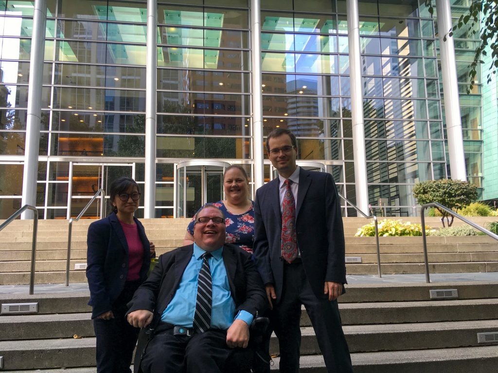 Four people in front of a courthouse entrance, smiling at camera.