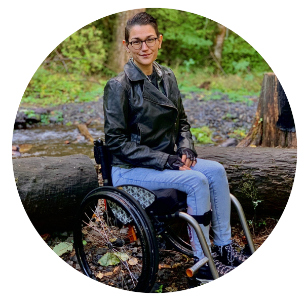 A woman sits in a wheelchair, wearing black leather jacket and jeans.