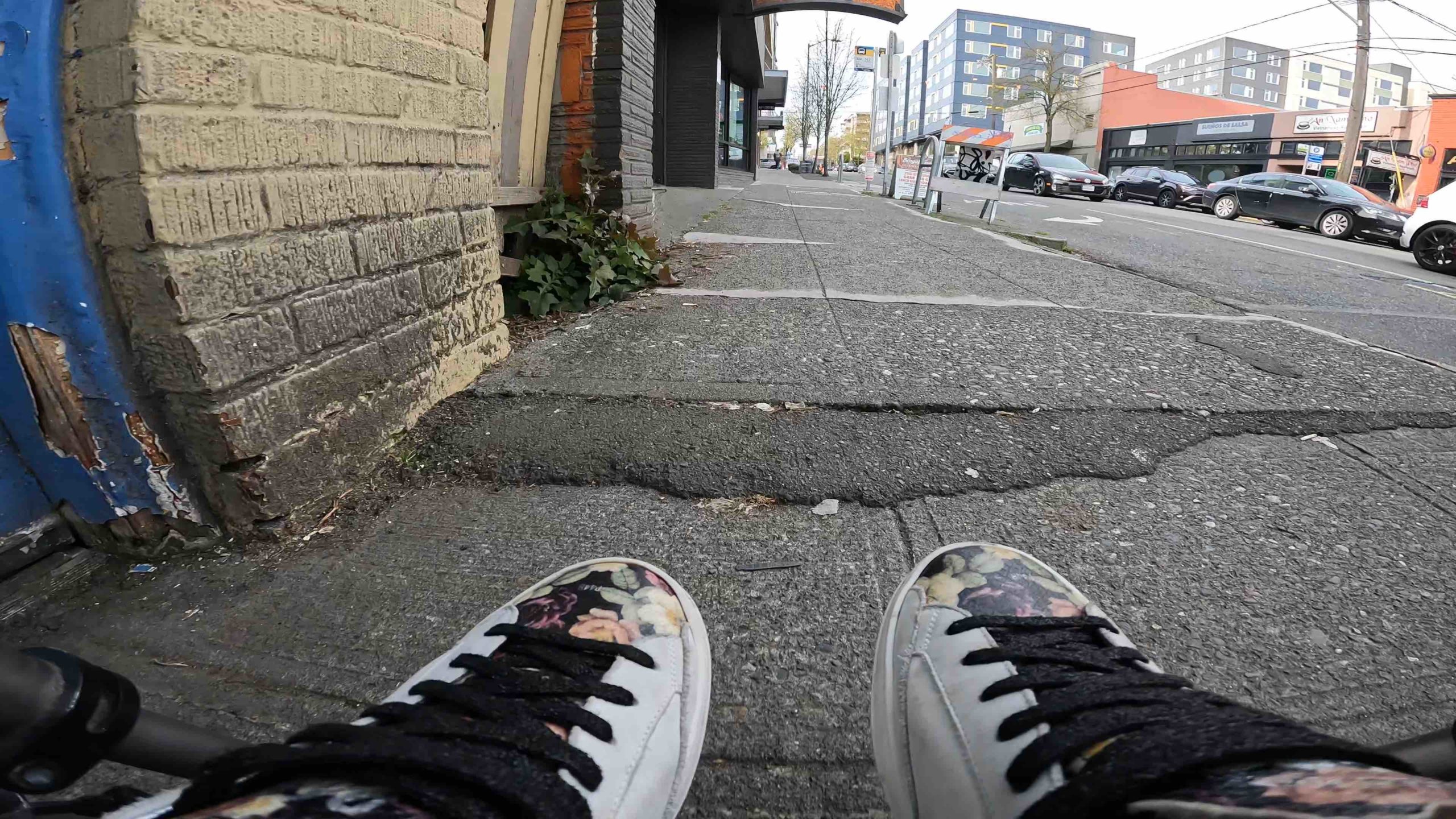 an image of a cracked sidewalk viewed through shoes from the POV of someone in a wheelchair