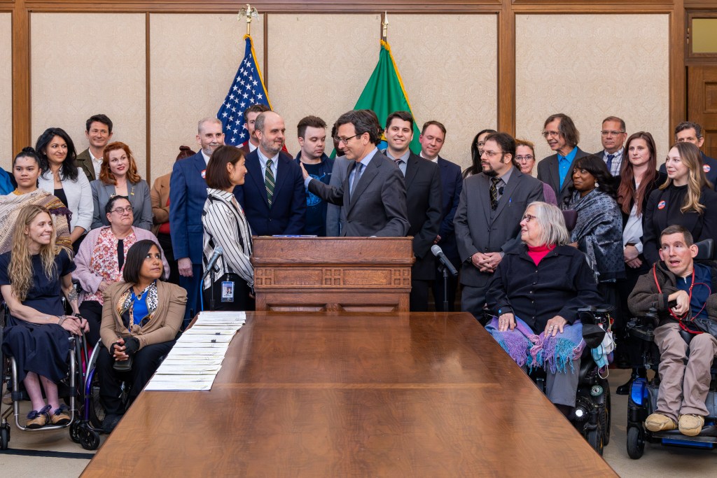 A group of people of mixed abilities gather around Governor Ferguson in the state capitol